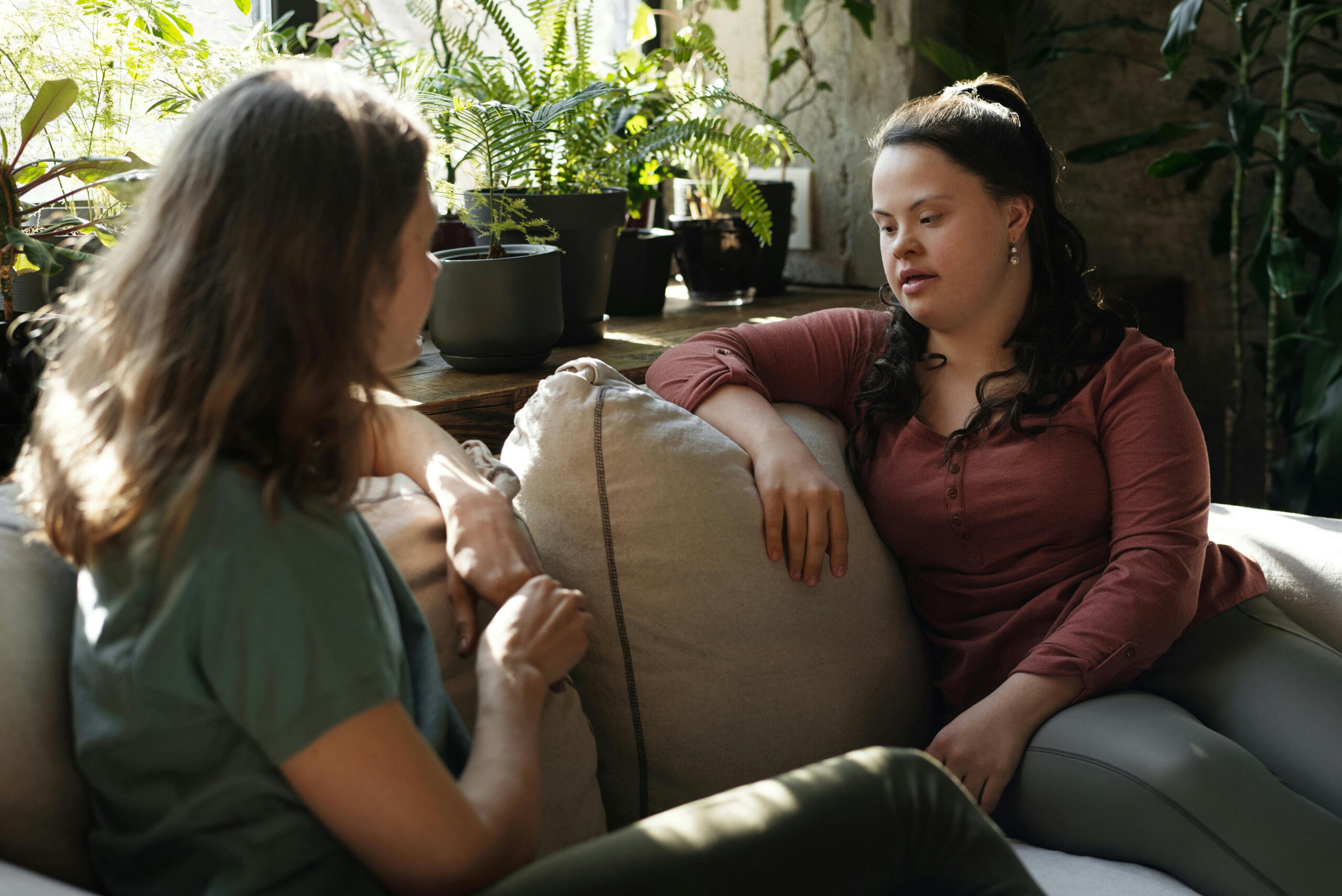 Two people sat on a sofa chatting with plants surrounding them